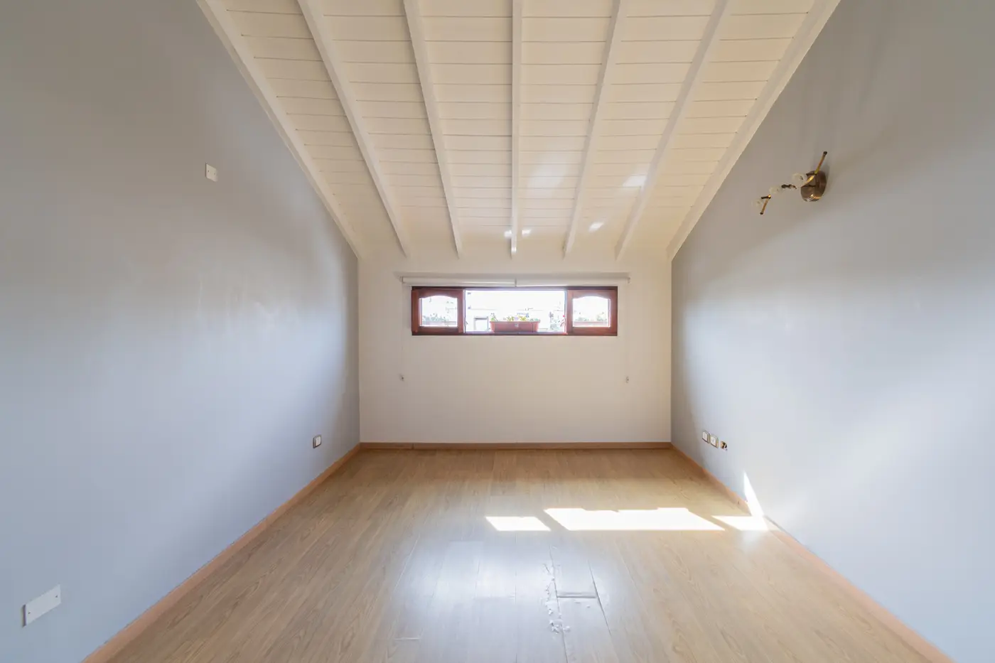Altillo vacío con techo de madera blanca y una ventana chica